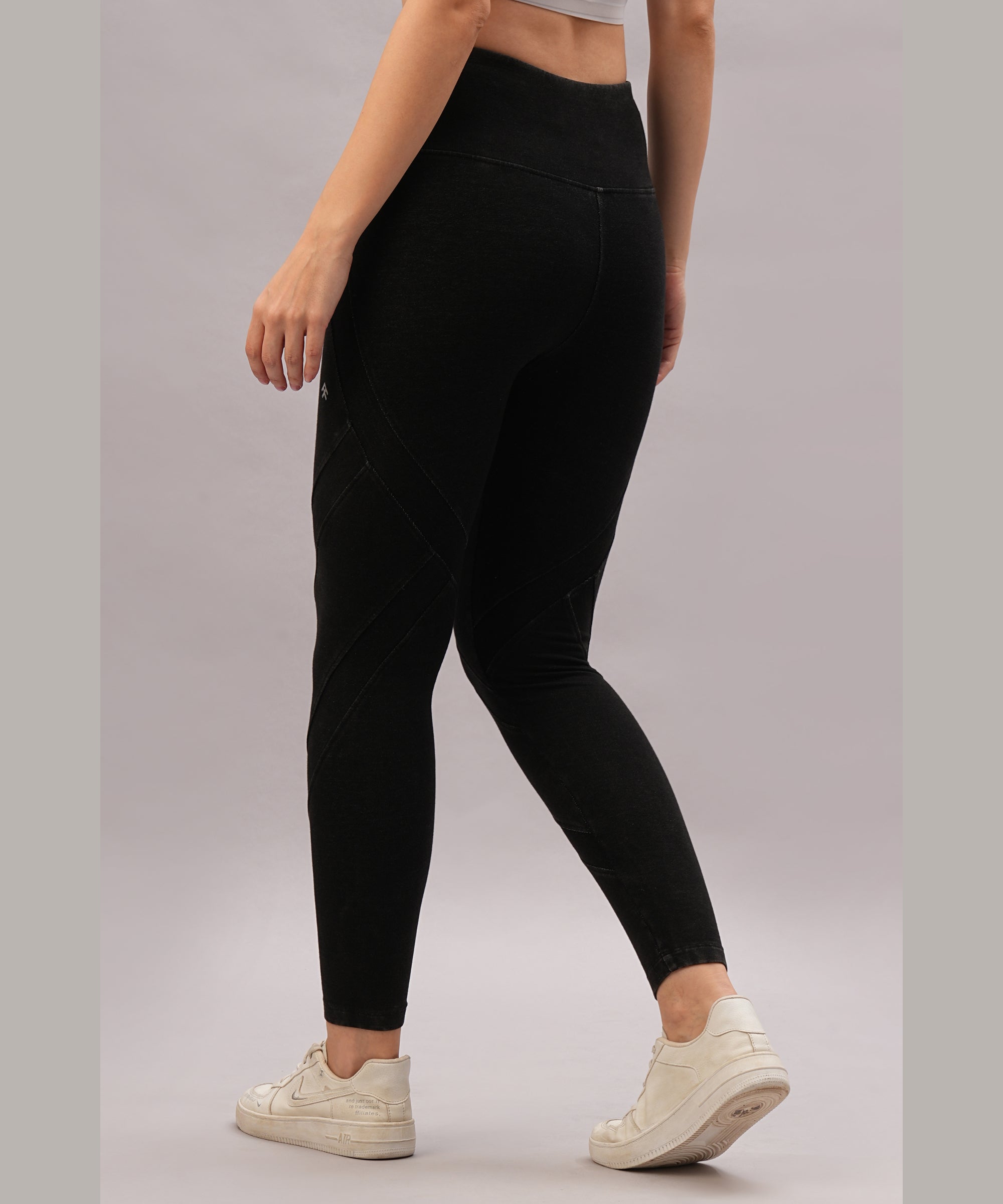 A woman models Black Denim Wash Leggings featuring a high-rise waistband and pairs them with white sneakers, posed against a neutral background.