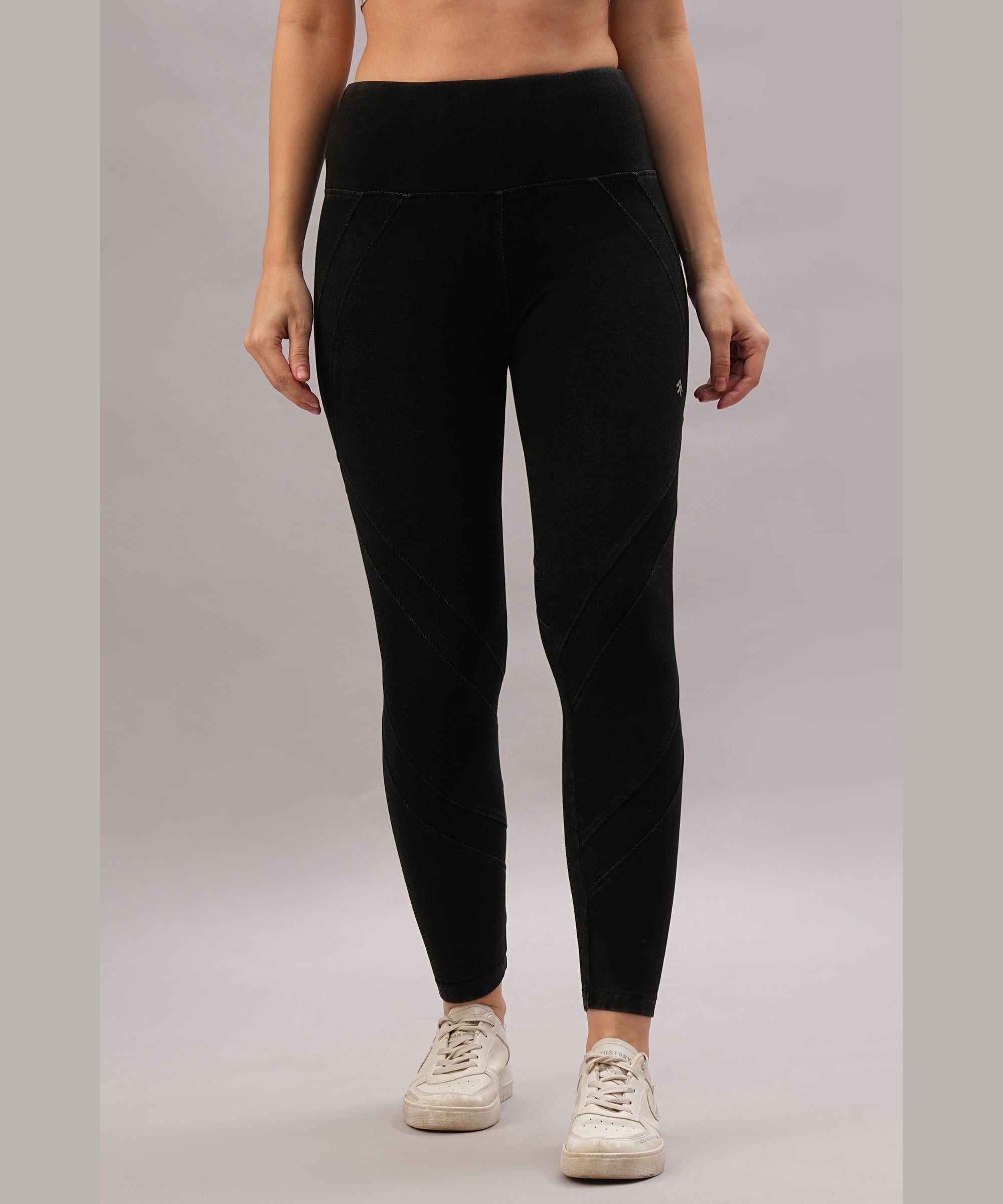 A person stands against a plain gray background wearing Black Denim Wash Leggings with a high-rise waistband and white sneakers.