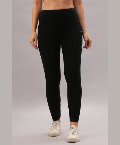A person stands against a plain gray background wearing Black Denim Wash Leggings with a high-rise waistband and white sneakers.