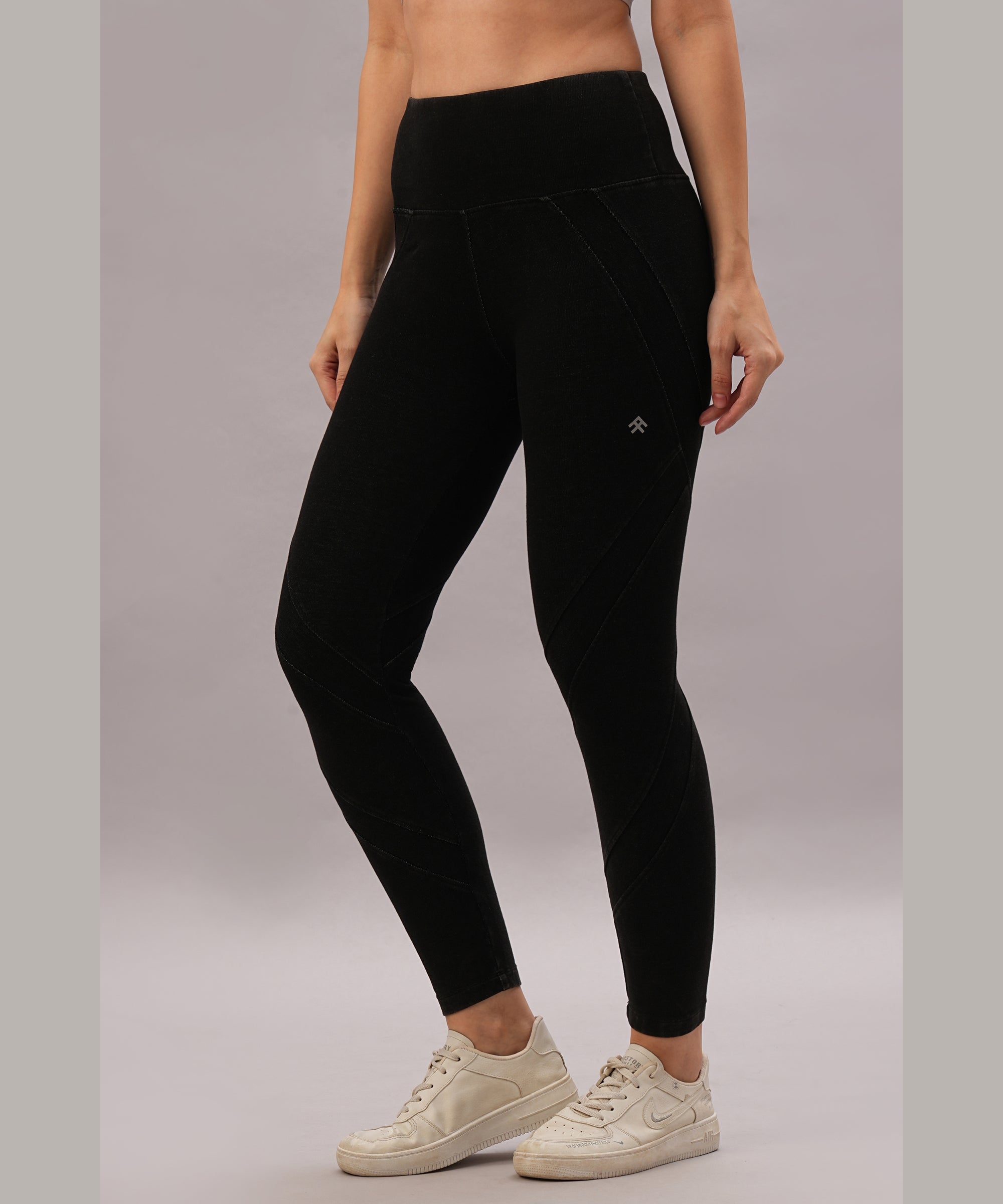 A person models Black Denim Wash Leggings featuring a high-rise waistband, paired with white sneakers, while standing against a plain background.