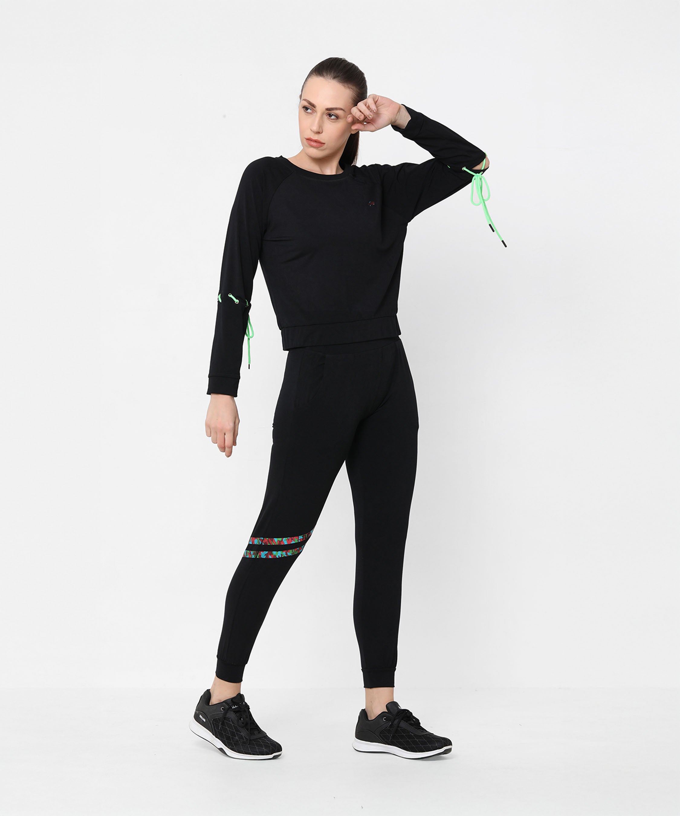A woman poses against a plain white background wearing the Black Sweatshirt With Joggers, featuring iridescent camo tape accents and paired with sneakers.