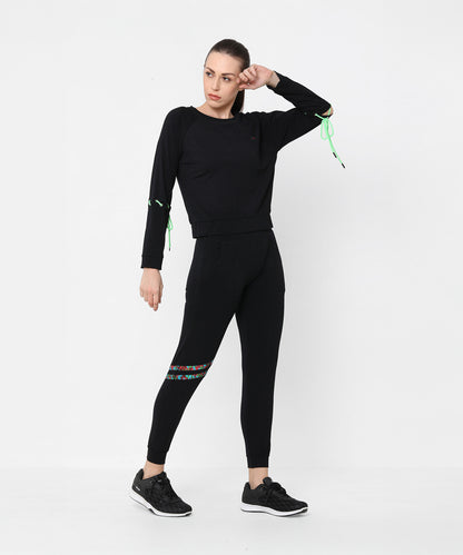 A woman poses against a plain white background wearing the Black Sweatshirt With Joggers, featuring iridescent camo tape accents and paired with sneakers.