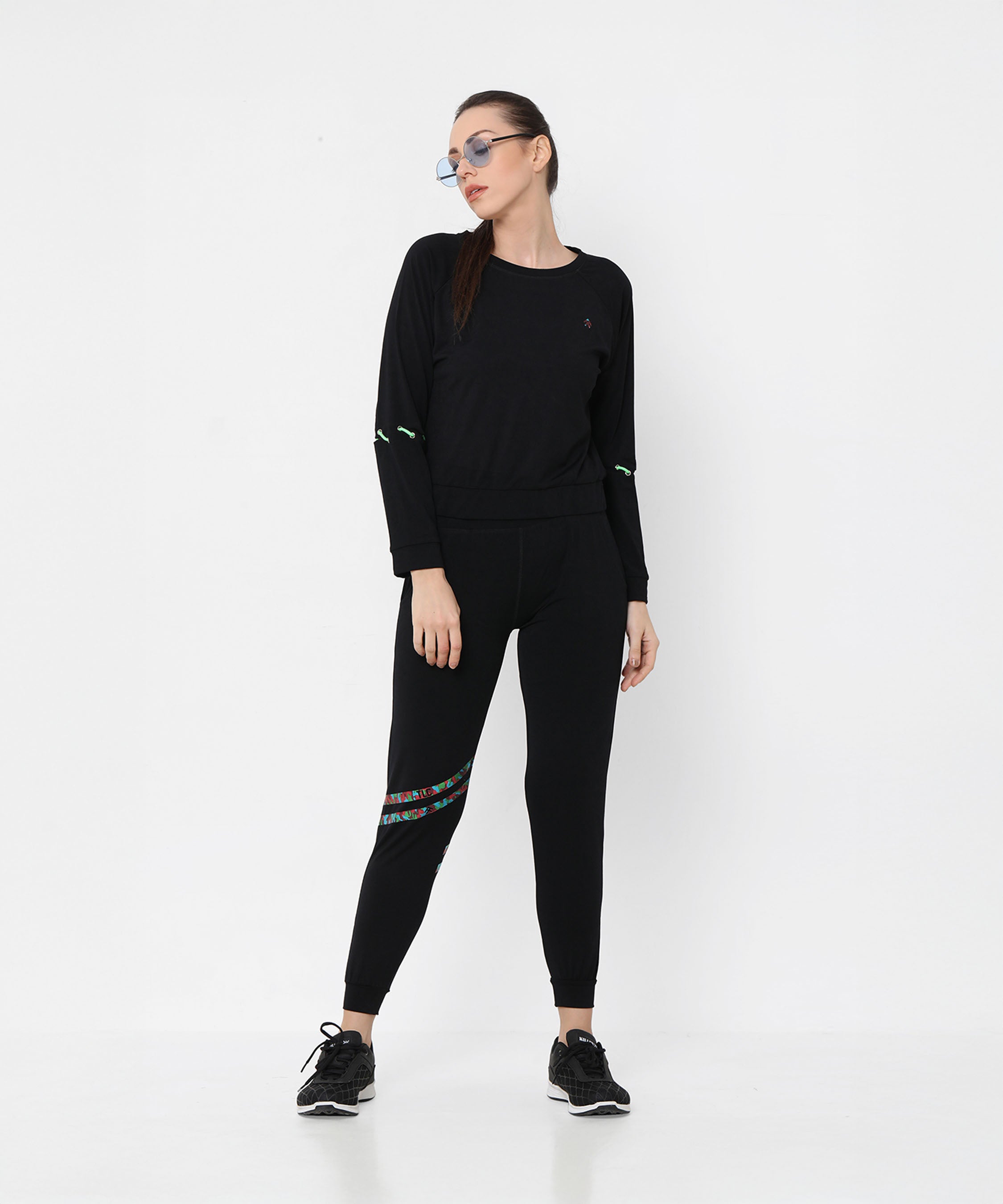 Woman wearing Black Sweatshirt With Joggers, featuring iridescent camo tape and sneakers, poses against a plain white background.
