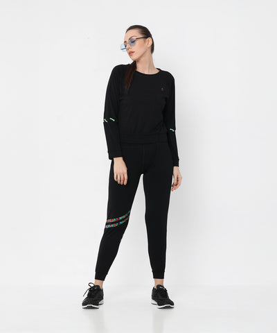Woman wearing Black Sweatshirt With Joggers, featuring iridescent camo tape and sneakers, poses against a plain white background.
