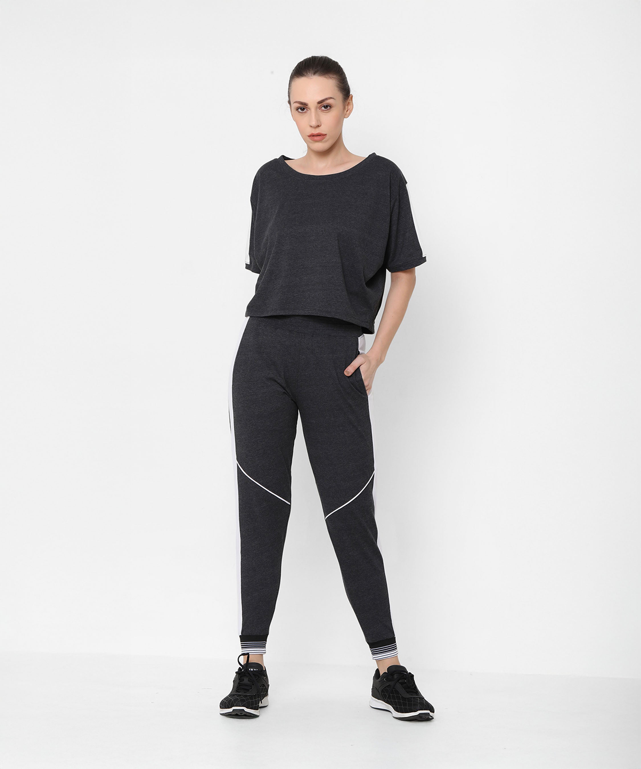 Woman wears the Melange Dark Grey Set—comfort fit top and joggers paired with black sneakers—standing against a plain white background.