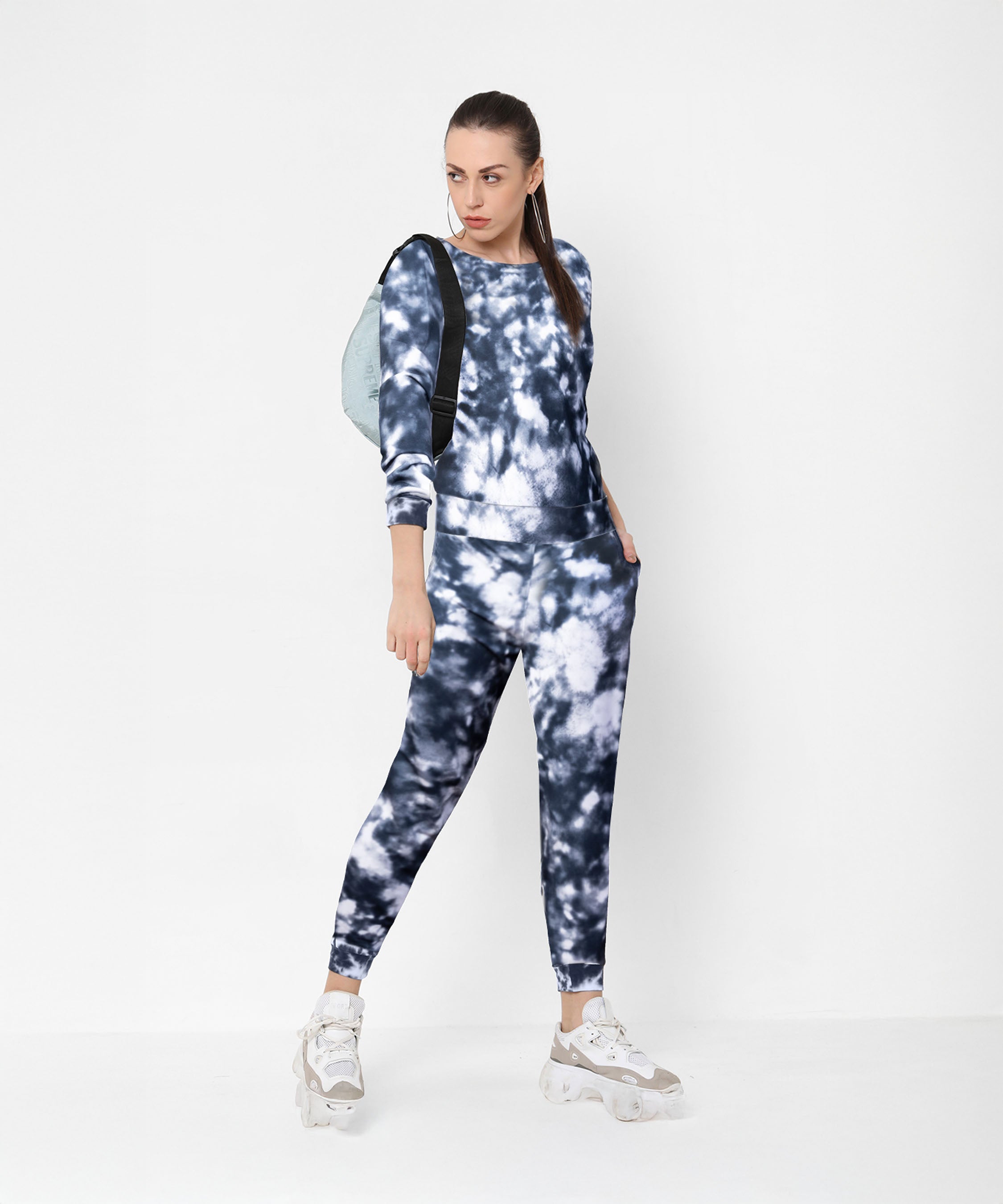 A woman wearing the Tie and Dye Tracksuit Set, white sneakers, and a backpack poses stylishly against a white background.
