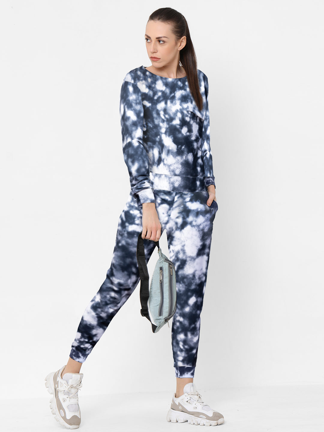 A woman in a black and white Tie and Dye Tracksuit Set holds a light blue backpack while standing against a white background, showcasing her elevated fashion style.