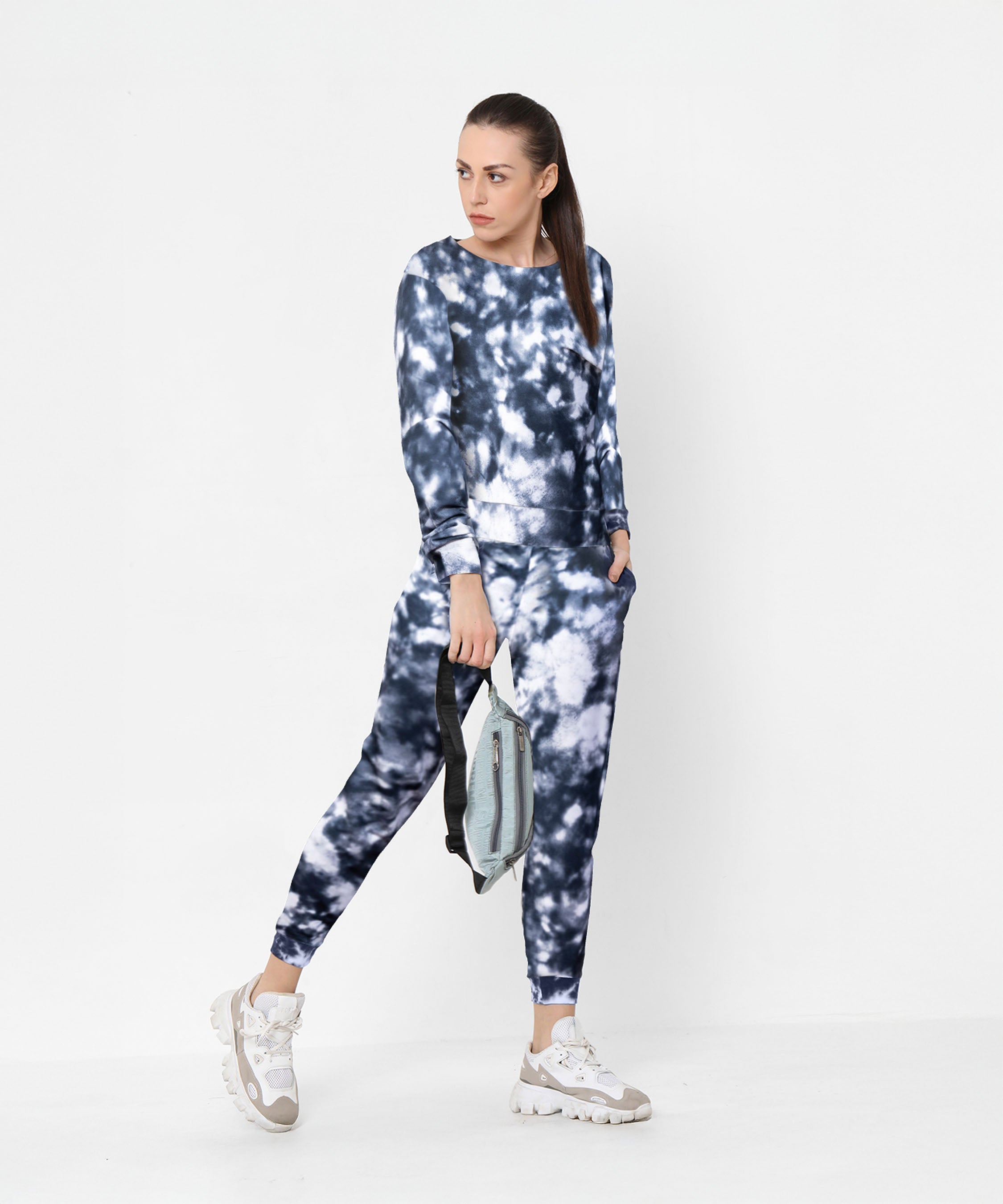 Woman wearing the Tie and Dye Tracksuit Set in blue and white, featuring signature joggers, holding a bag against a plain white background.
