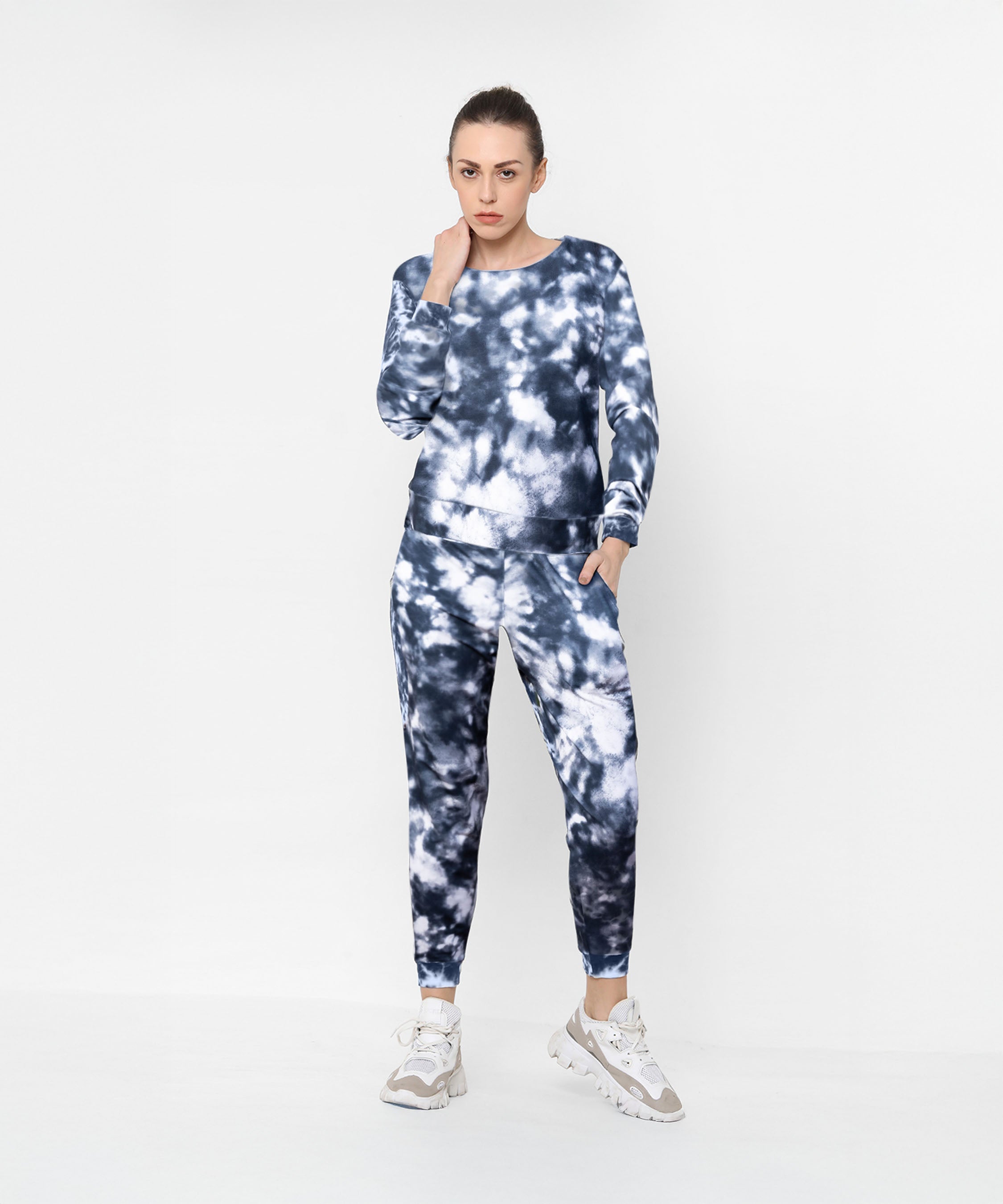 Woman in the Tie and Dye Tracksuit Set—featuring a stylish black and white design—paired with white sneakers, standing against a plain background. This look defines effortless fashion at its finest.