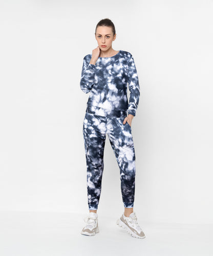 Woman in the Tie and Dye Tracksuit Set—featuring a stylish black and white design—paired with white sneakers, standing against a plain background. This look defines effortless fashion at its finest.