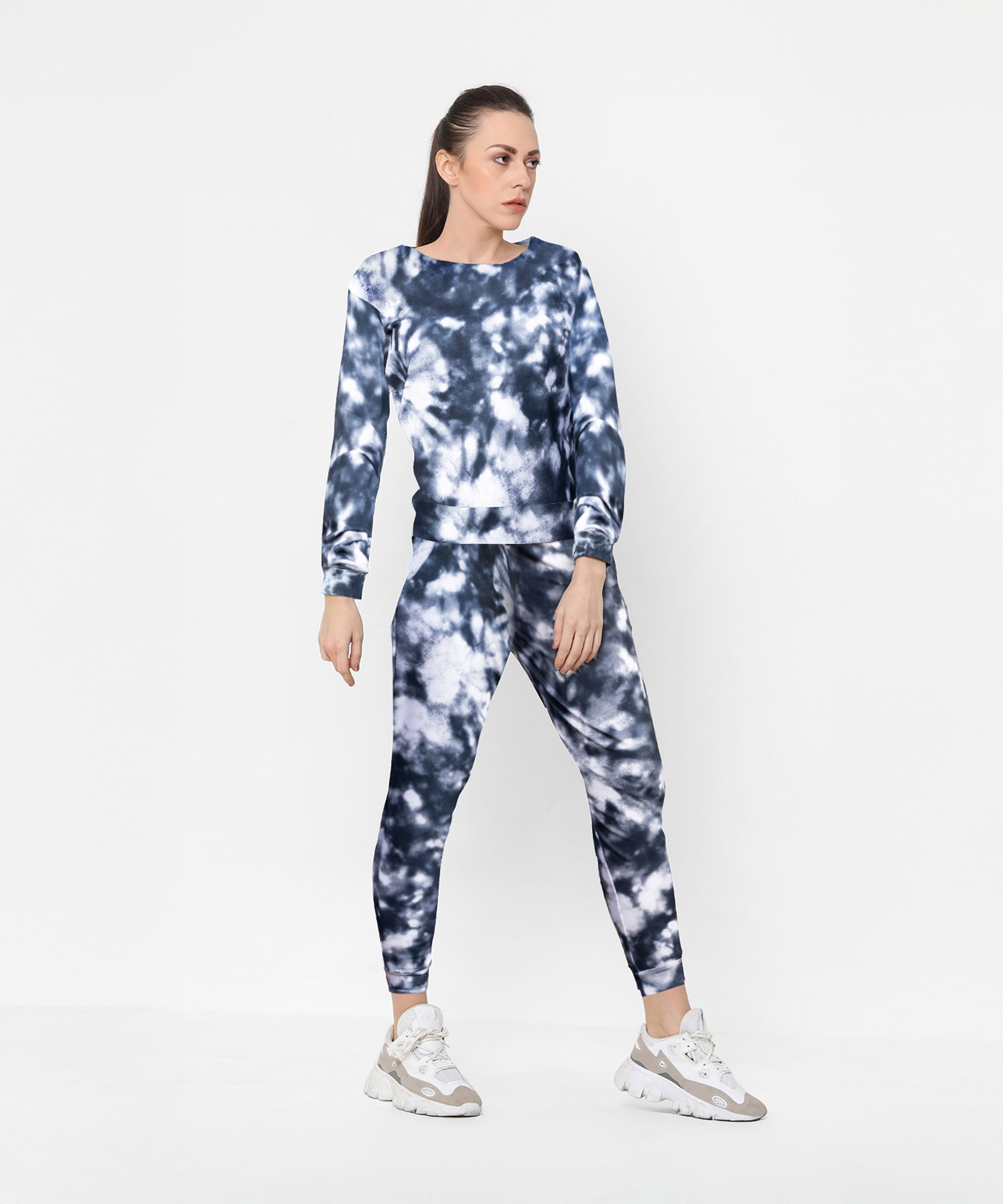 Woman wearing a Tie and Dye Tracksuit Set with white sneakers, standing against a white background.