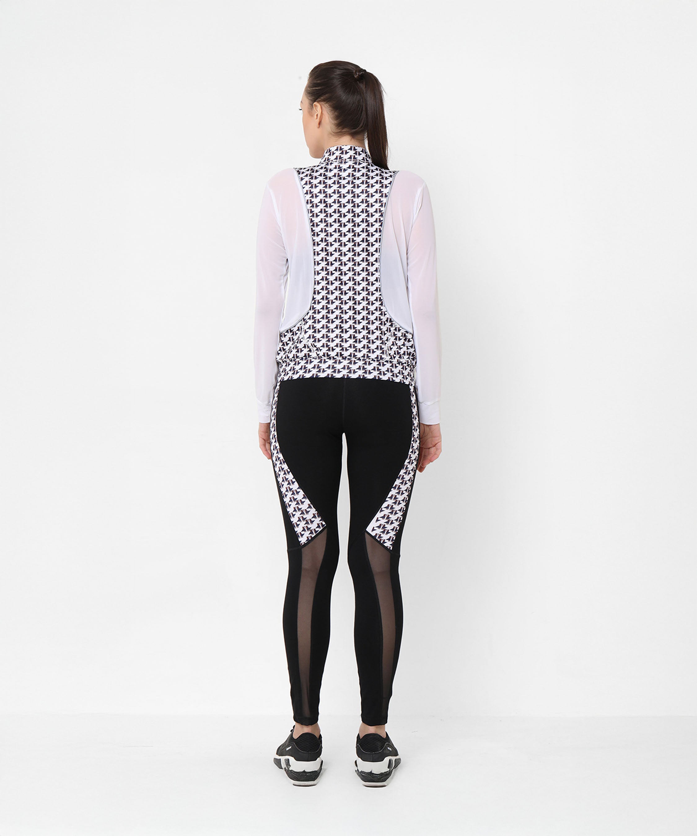 Woman facing away in athleisure style, wearing the Esther Jacket With Leggings—a printed net jacket with mesh sleeves and matching black leggings featuring sleek mesh panels.