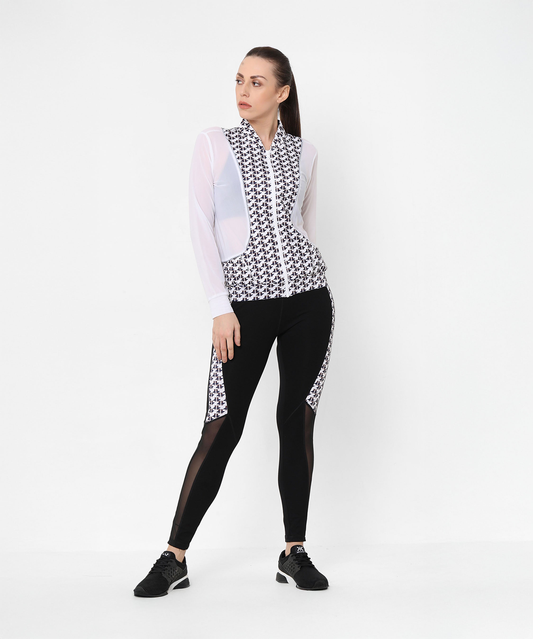 Confident woman in athleisure, wearing the Esther Jacket With Leggings—a printed net jacket with sheer sleeves and matching black leggings—paired with black sneakers.