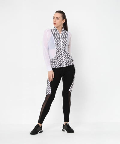 Confident woman in athleisure, wearing the Esther Jacket With Leggings—a printed net jacket with sheer sleeves and matching black leggings—paired with black sneakers.