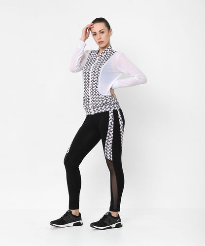 A woman poses confidently in the Esther Jacket With Leggings athleisure set, wearing a stylish black and white printed net jacket with matching leggings.