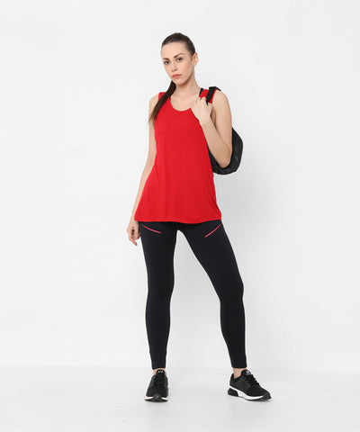 Woman in a Red Tank Top With Overlap Back, black leggings, and sneakers, carrying a backpack, standing against a white background.