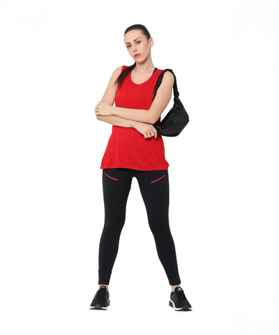 A woman in a red tank top, Black Leggings With Zip, sneakers, and a black bag on her shoulder stands with arms crossed.