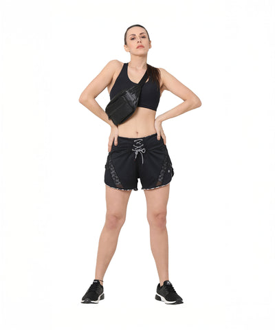 Woman poses confidently in Sammy mesh shorts with a tie-up waistband and black sportswear, hands on hips, against a white background.