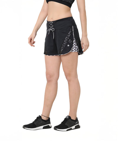 Woman wearing Sammy mesh shorts with a tie-up waistband, a black sports bra, and black sneakers, standing against a white background.