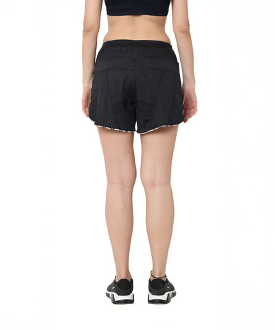 A woman in Sammy mesh shorts with a tie-up waistband, a black top, and sneakers stands facing away against a white background.