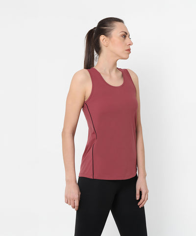 A woman stands sideways against a plain white background wearing a Punch Pink Racer Back Top with a mesh panel and black pants.