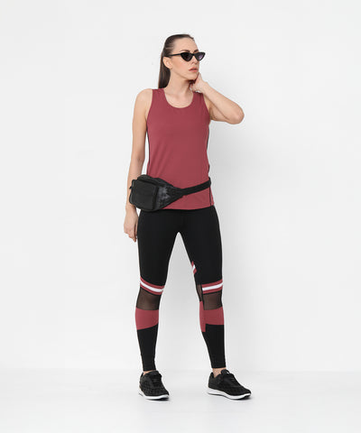 A woman in sunglasses and black mesh leggings stands against a white wall, wearing the Punch Pink Racer Back Top and a black waist bag.