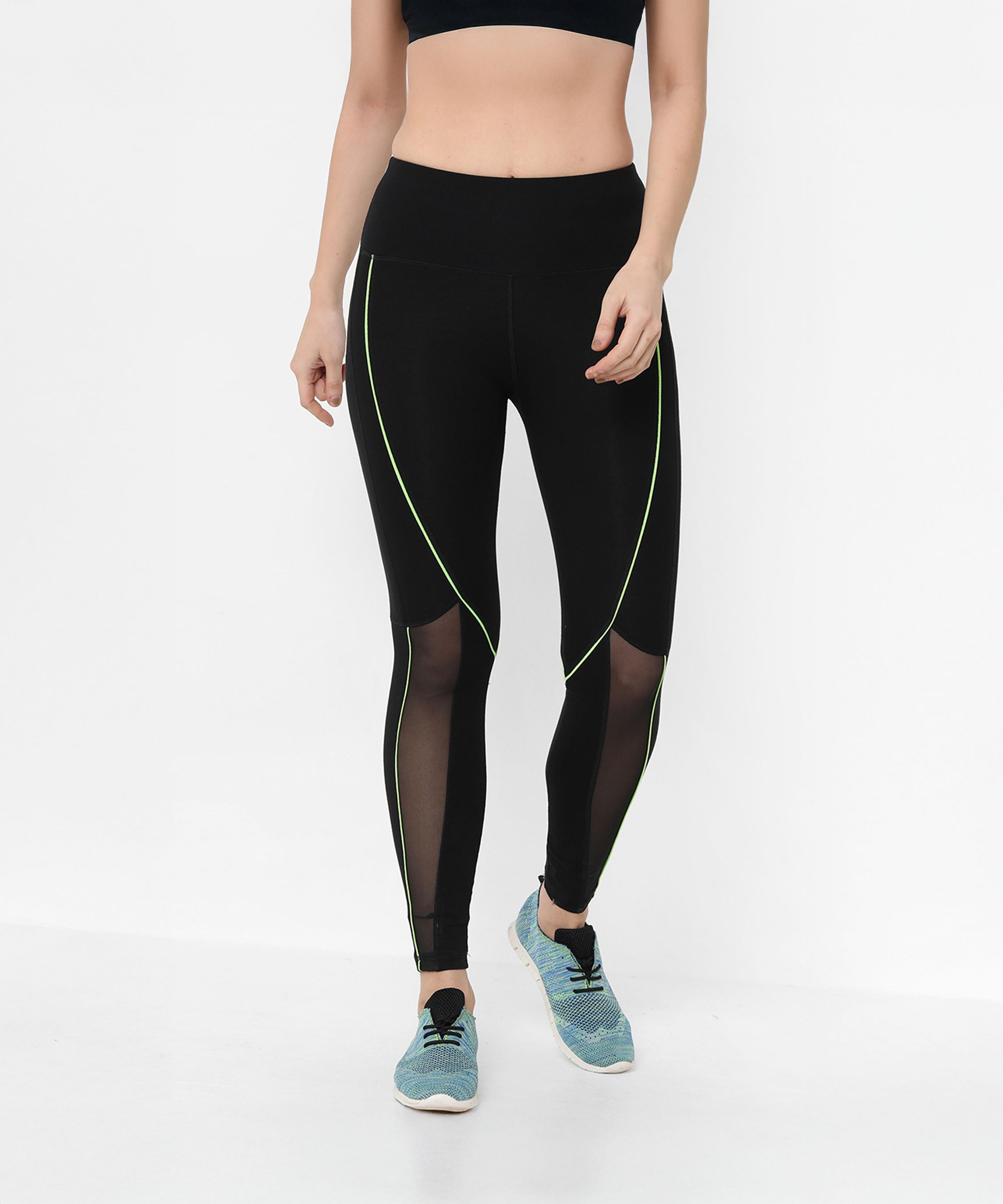 Woman wearing Fab Fit Neon Pop Leggings featuring black mesh fabric with neon green piping and a high-rise waistband, styled with a black crop top and blue sneakers.