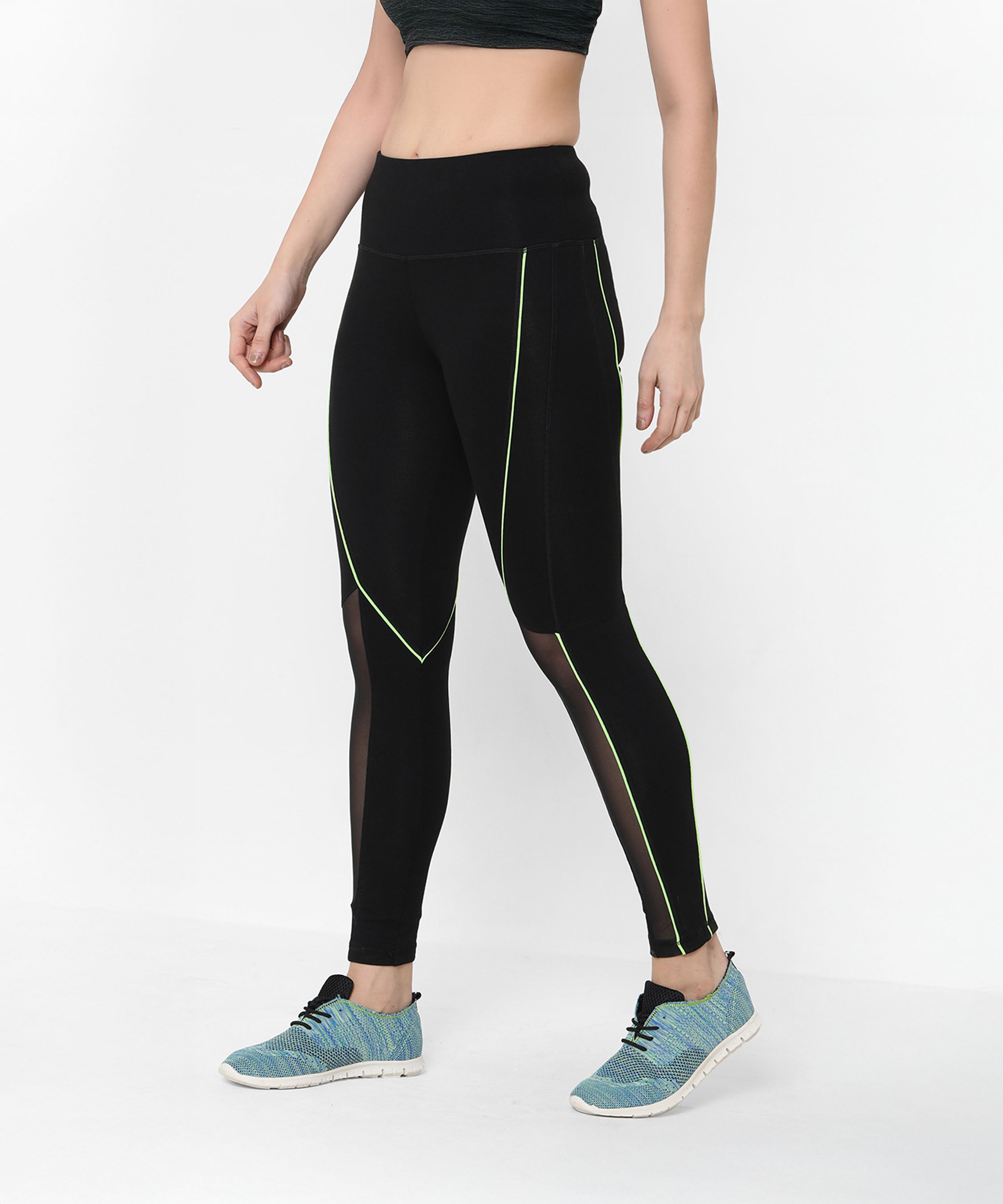 A woman wears the Fab Fit Neon Pop Leggings featuring black mesh, green piping, and a high-rise waistband, paired with blue sneakers and a dark crop top.