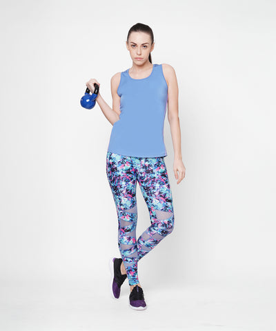 Woman in Nyla racer back top and colorful leggings with an athletic look, holding a small kettlebell against a white background.