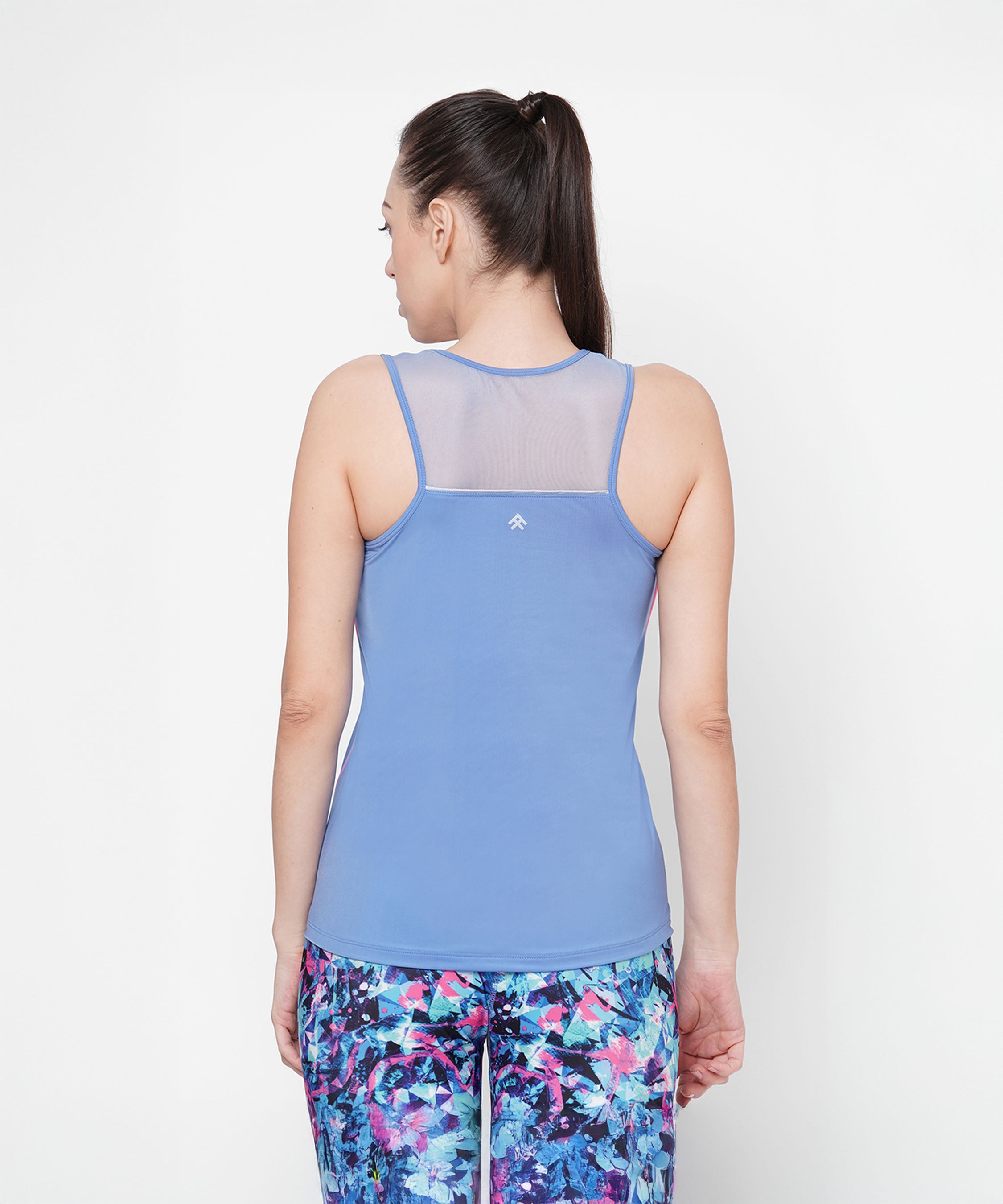 A woman with a ponytail, wearing the Nyla racer back top and colorful leggings, stands with her back to the camera, highlighting an athletic look.
