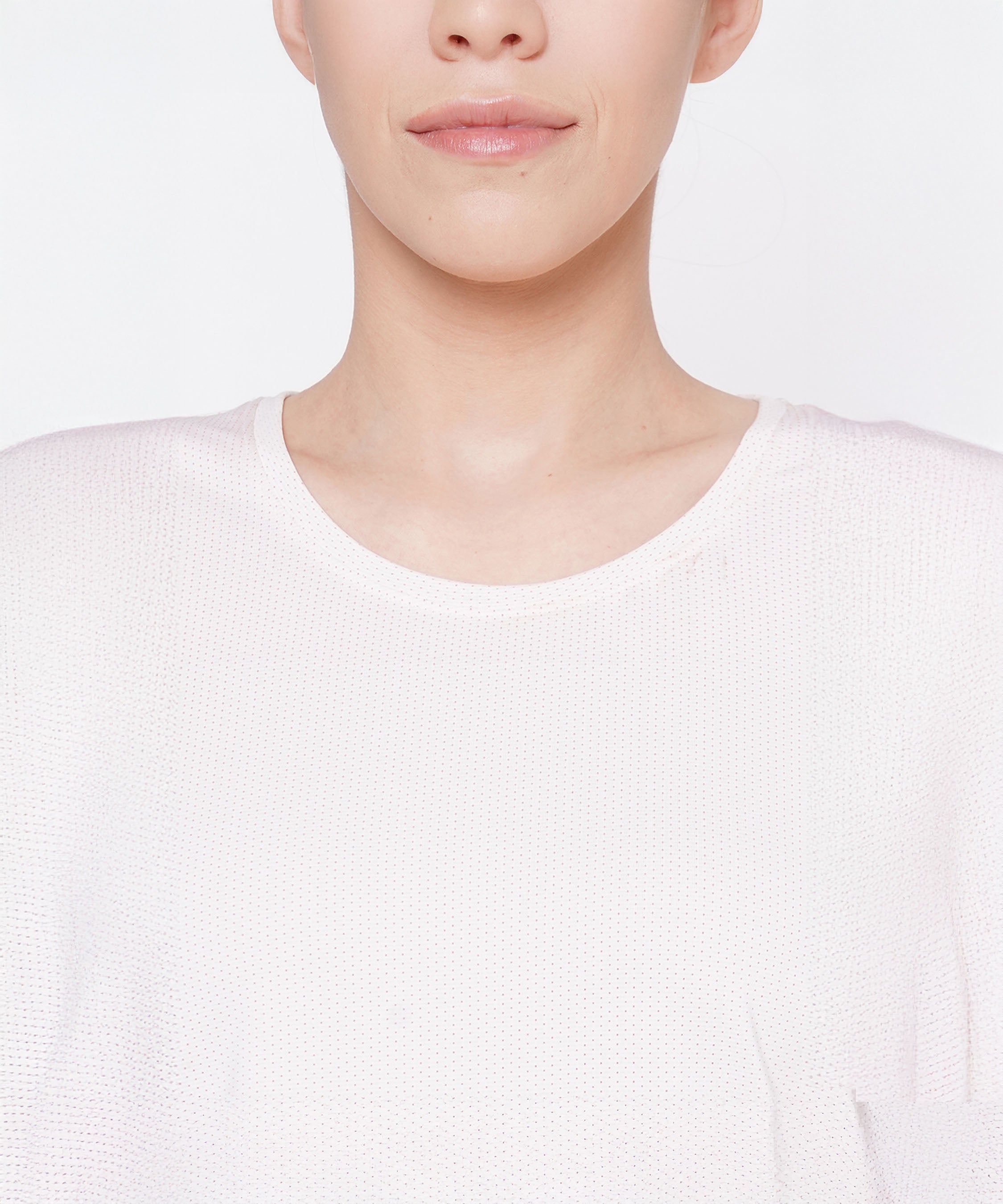 A woman wearing a light pink round neck T-shirt made of moisture-wicking mesh fabric, shown from the shoulders up with a neutral facial expression.