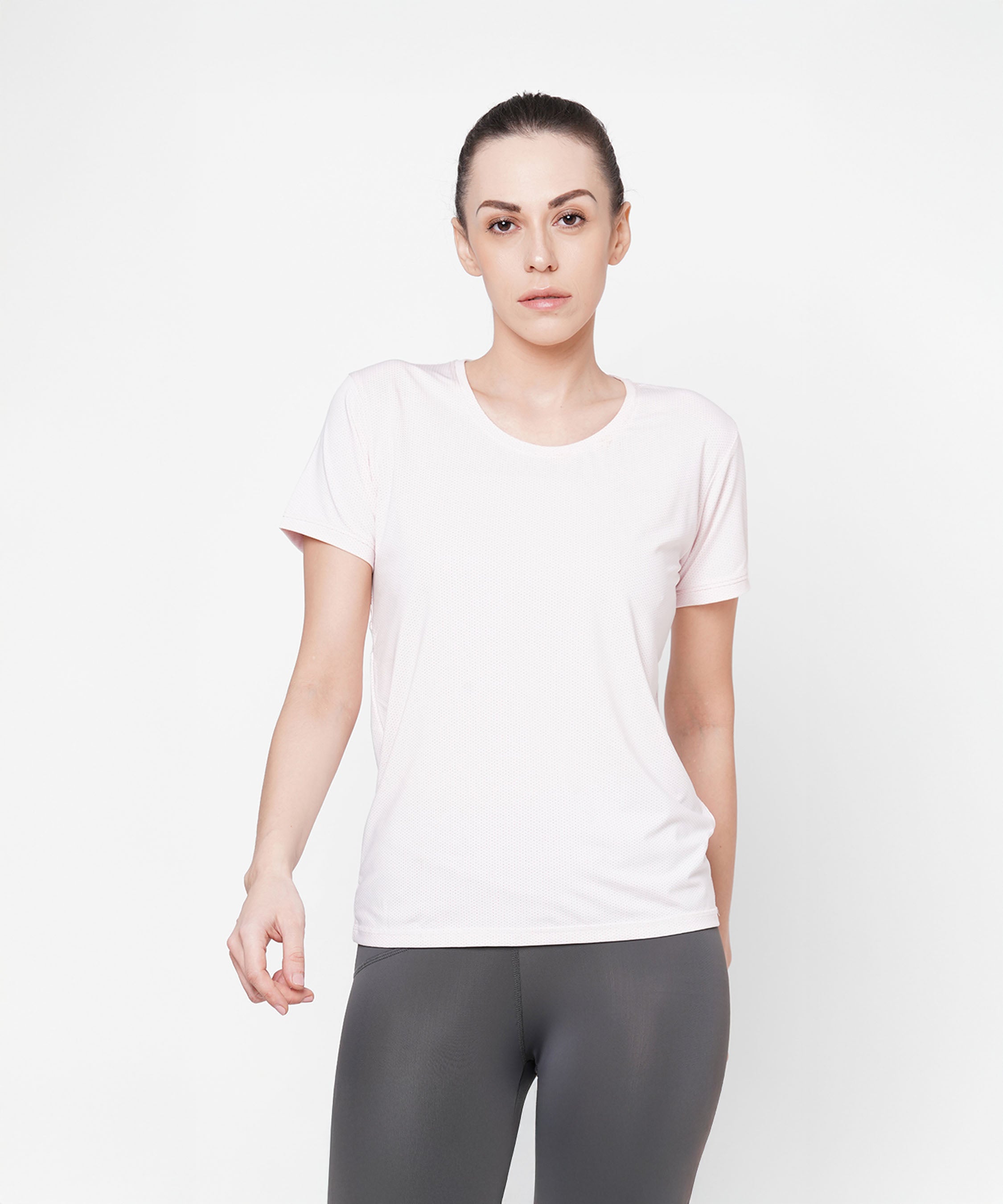 A woman in a plain light pink round neck T-shirt and gray leggings stands against a white background.