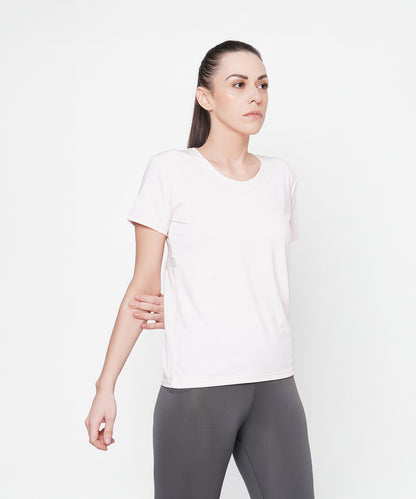 A woman wears a Light Pink Round Neck T-Shirt and gray pants against a white background. The shirt’s moisture-wicking mesh fabric keeps her cool and comfortable during any activity.
