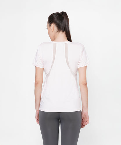 A woman stands with her back to the camera, wearing a Light Pink Round Neck T-Shirt and gray leggings against a white background.