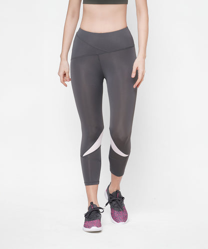 Woman wearing Classic Capri dark gray high-waisted leggings with a thick waistband and white accents, paired with pink sneakers, standing against a white background.