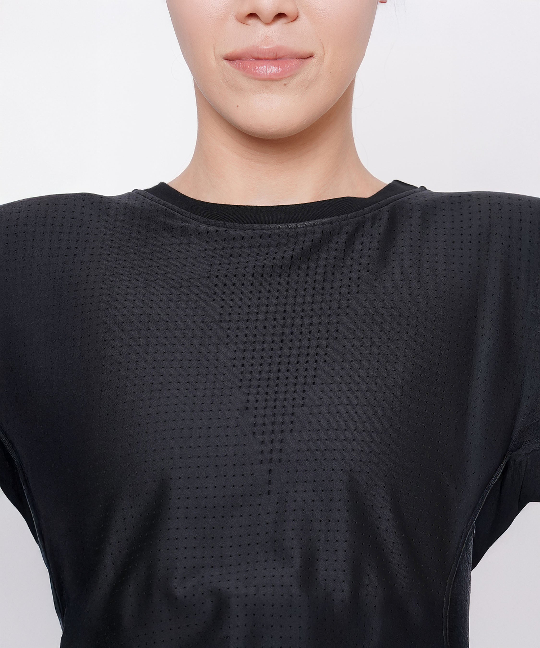 A woman models the Black Crop Top With Mesh Overlay, shown from the shoulders up with a neutral expression.