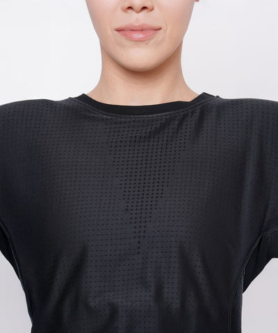 A woman models the Black Crop Top With Mesh Overlay, shown from the shoulders up with a neutral expression.