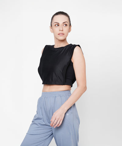Woman in athletic wear looks to the side, wearing the Black Crop Top With Mesh Overlay and light blue pants against a white background.