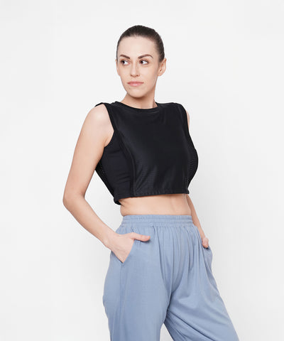 Woman wearing a Black Crop Top With Mesh Overlay and light blue pants, hands in pockets, looking to the side.