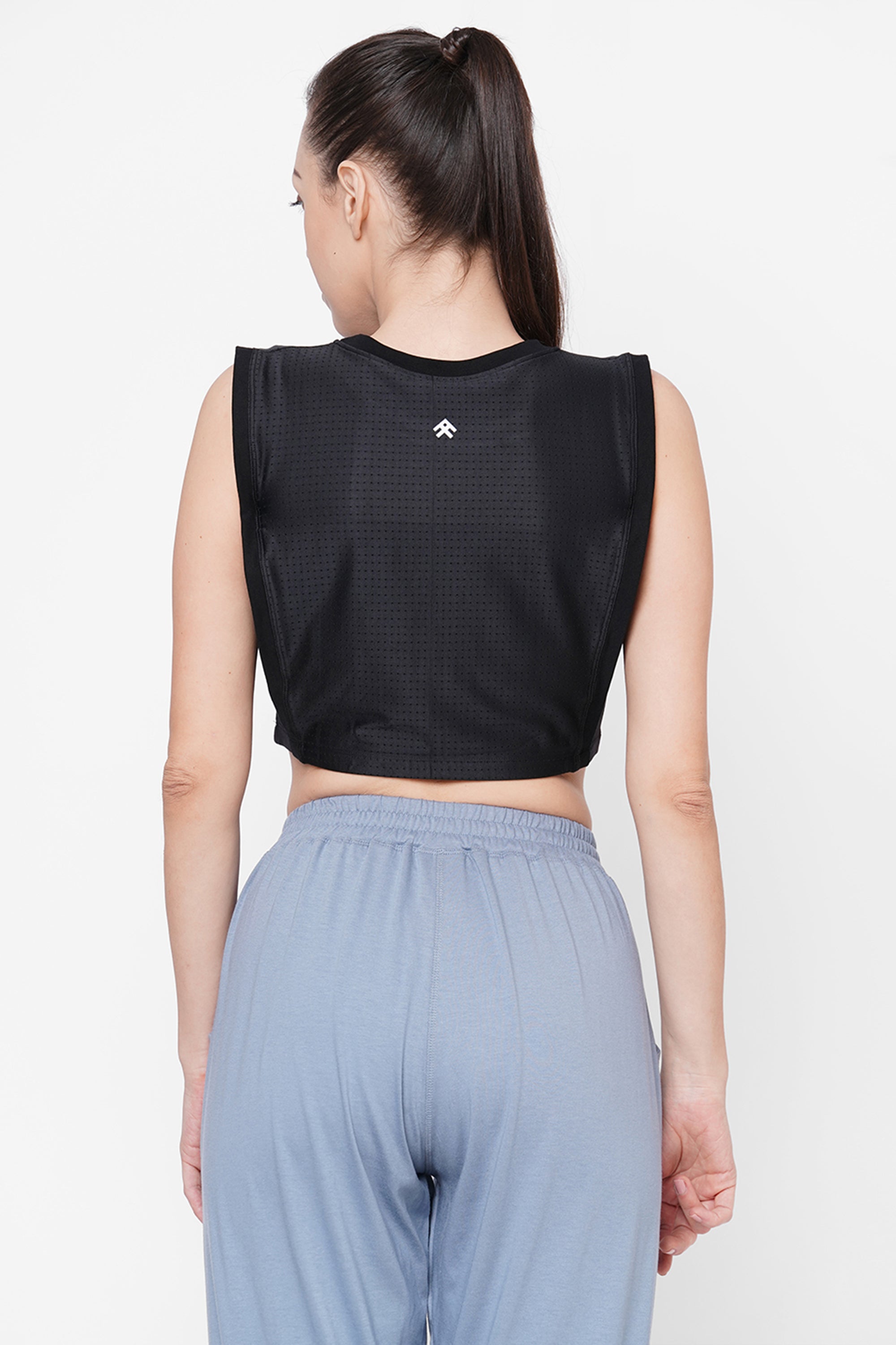 Woman with a ponytail shown from the back, wearing a Black Crop Top With Mesh Overlay and light blue pants.