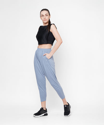 Woman in a black crop top and grey yoga pants stands with one hand in her pocket, looking to the side.