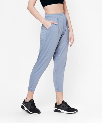 Person wearing grey yoga pants, black crop top, and black sneakers, with one hand in pocket.