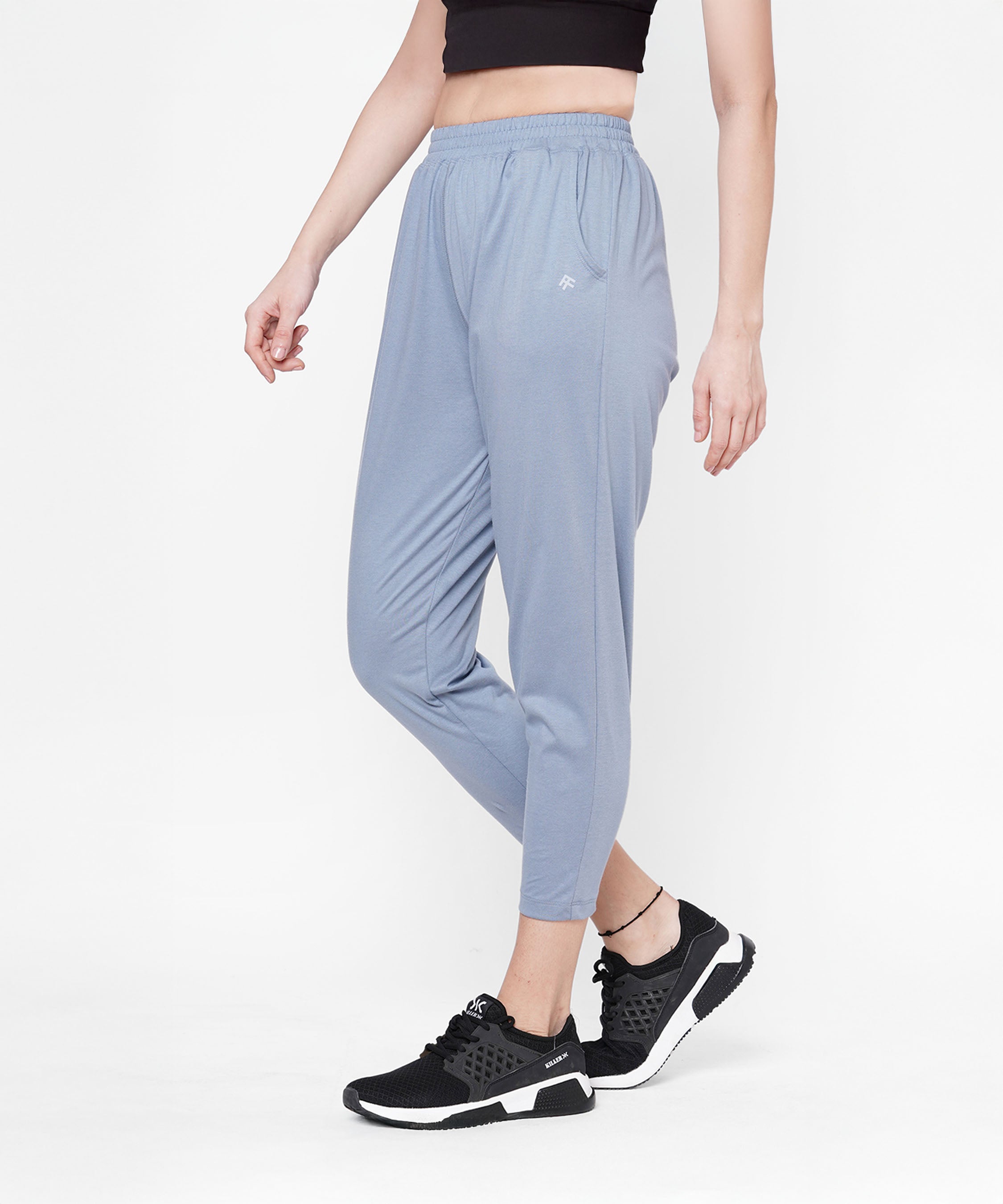 Woman wearing grey yoga pants, a black crop top, and black sneakers, standing against a white background.