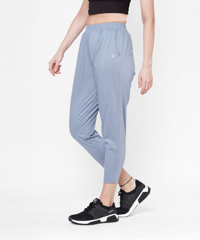 Woman wearing grey yoga pants, a black crop top, and black sneakers, standing against a white background.