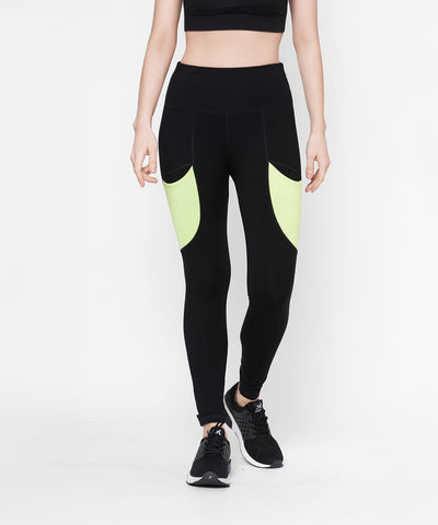 A woman is wearing Black Leggings With Neon Green Patch, featuring side panels and a high-rise waistband, paired with a black crop top and black running shoes.