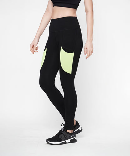 A woman in Black Leggings With Neon Green Patch, featuring a high-rise waistband and neon green patch pockets, pairs them with a black crop top and black sneakers while standing against a white background.