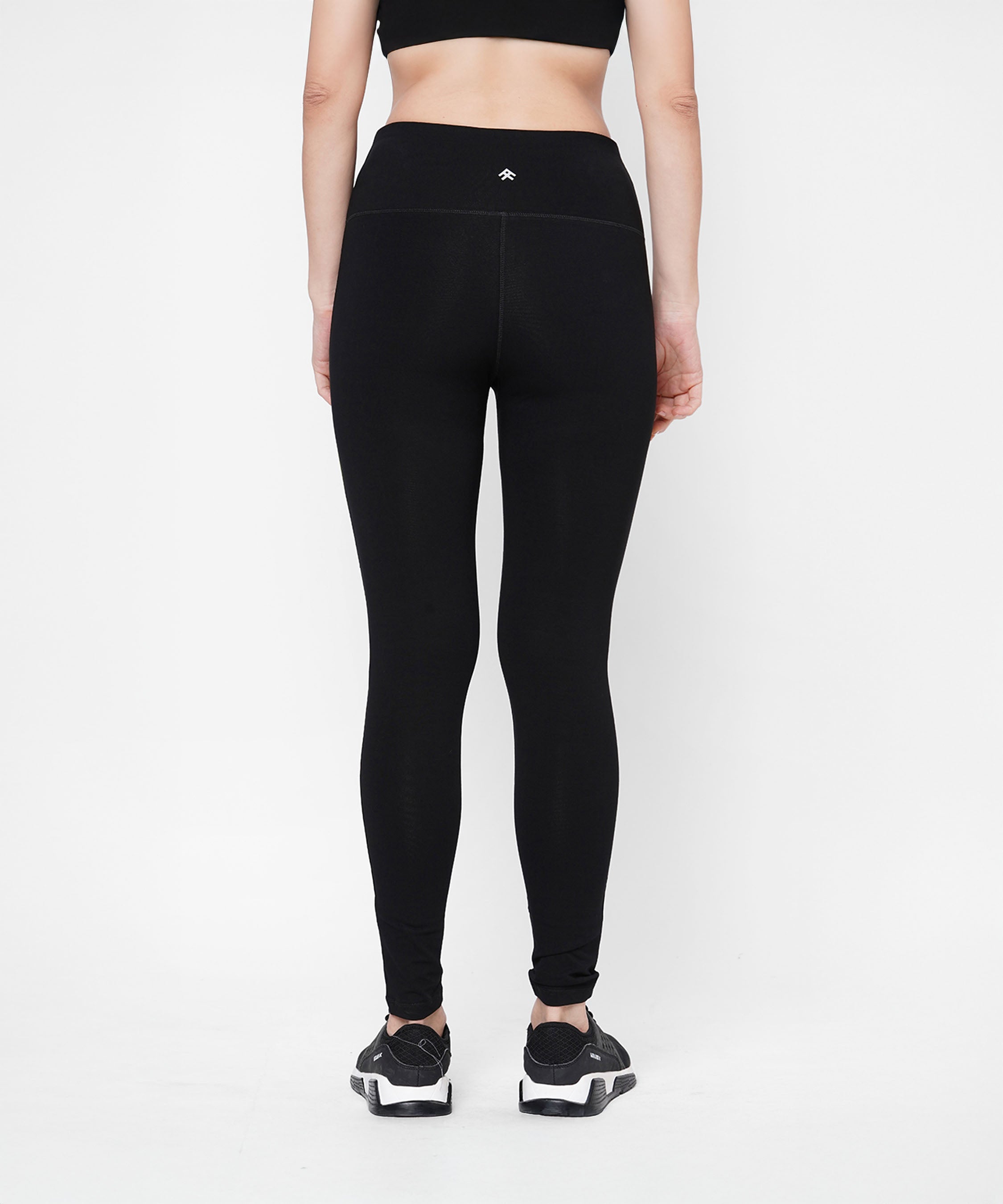 A woman stands with her back to the camera in Black Leggings With Neon Green Patch featuring a high-rise waistband, paired with a black sports bra, set against a white background.