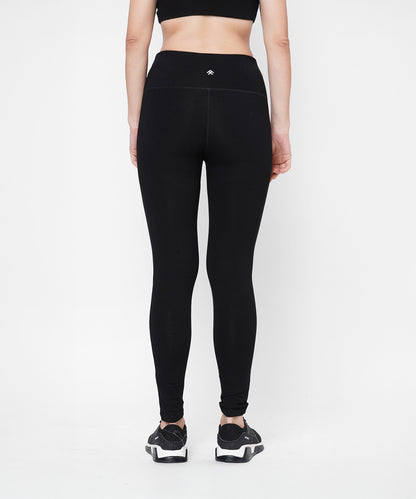 A woman stands with her back to the camera in Black Leggings With Neon Green Patch featuring a high-rise waistband, paired with a black sports bra, set against a white background.
