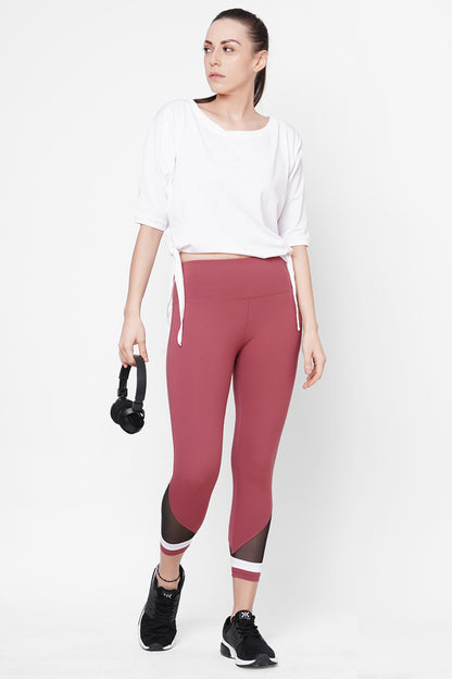 Woman in activewear holds headphones, wearing a white top and Punch Pink Capri featuring a compression-fit waistband—perfect workout clothing against a clean white background.