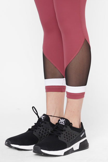 A person wears Punch pink Capri leggings with black mesh panels, a compression fit waistband, and black athletic sneakers on a white background—an ideal blend of comfort and style for workouts.